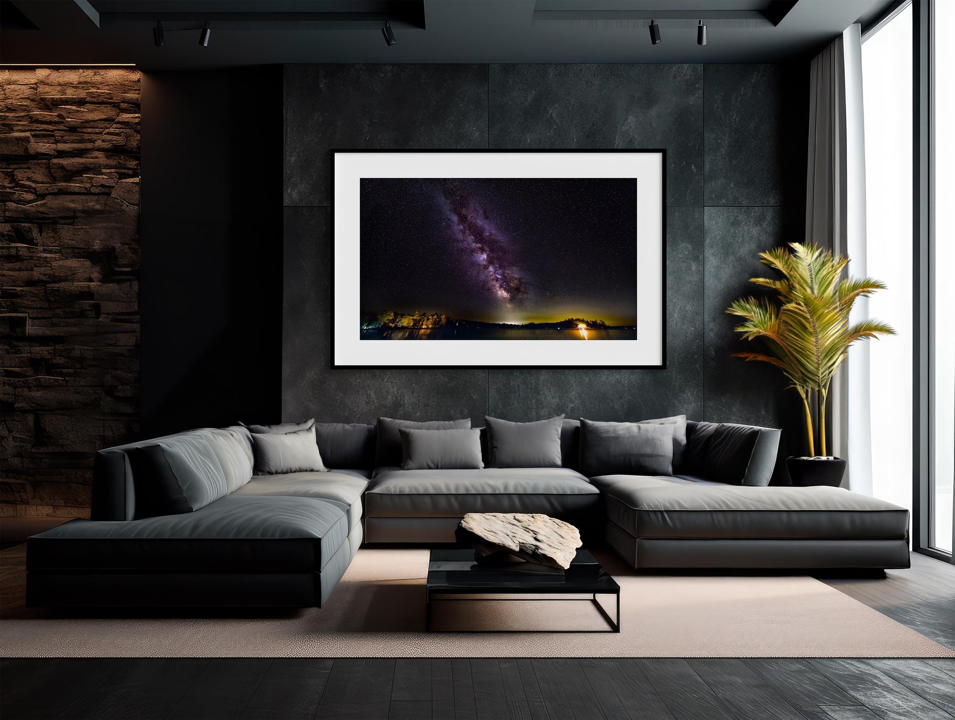 A vivid Milky Way core glows in a vertical sweep across a dark, starry night sky. The stars and galactic dust create a textured ribbon of light. Below, a calm lake mirrors faint reflections of the stars, with a rocky shoreline in the foreground and a glowing island of trees lit in the distance.