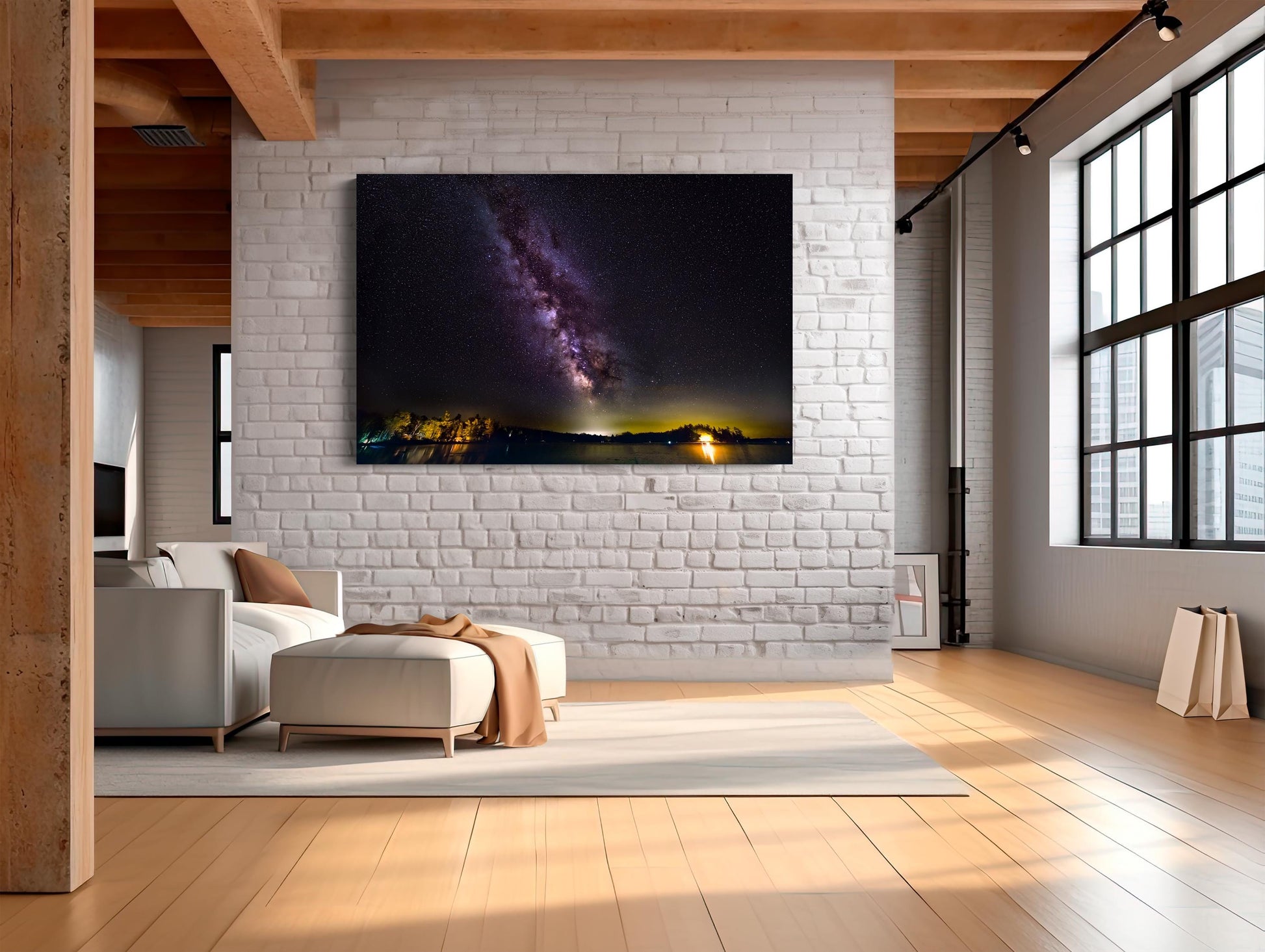 A vivid Milky Way core glows in a vertical sweep across a dark, starry night sky. The stars and galactic dust create a textured ribbon of light. Below, a calm lake mirrors faint reflections of the stars, with a rocky shoreline in the foreground and a glowing island of trees lit in the distance.