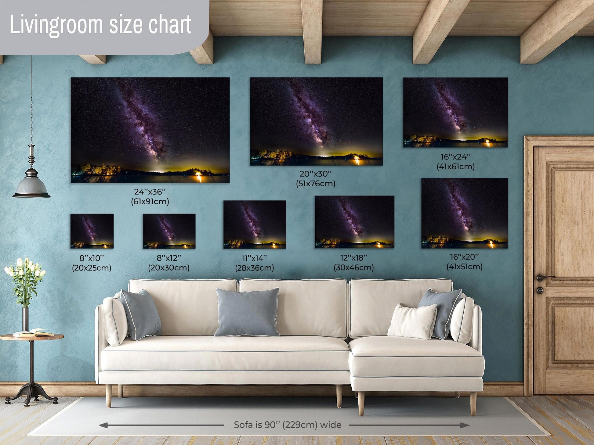 A vivid Milky Way core glows in a vertical sweep across a dark, starry night sky. The stars and galactic dust create a textured ribbon of light. Below, a calm lake mirrors faint reflections of the stars, with a rocky shoreline in the foreground and a glowing island of trees lit in the distance.