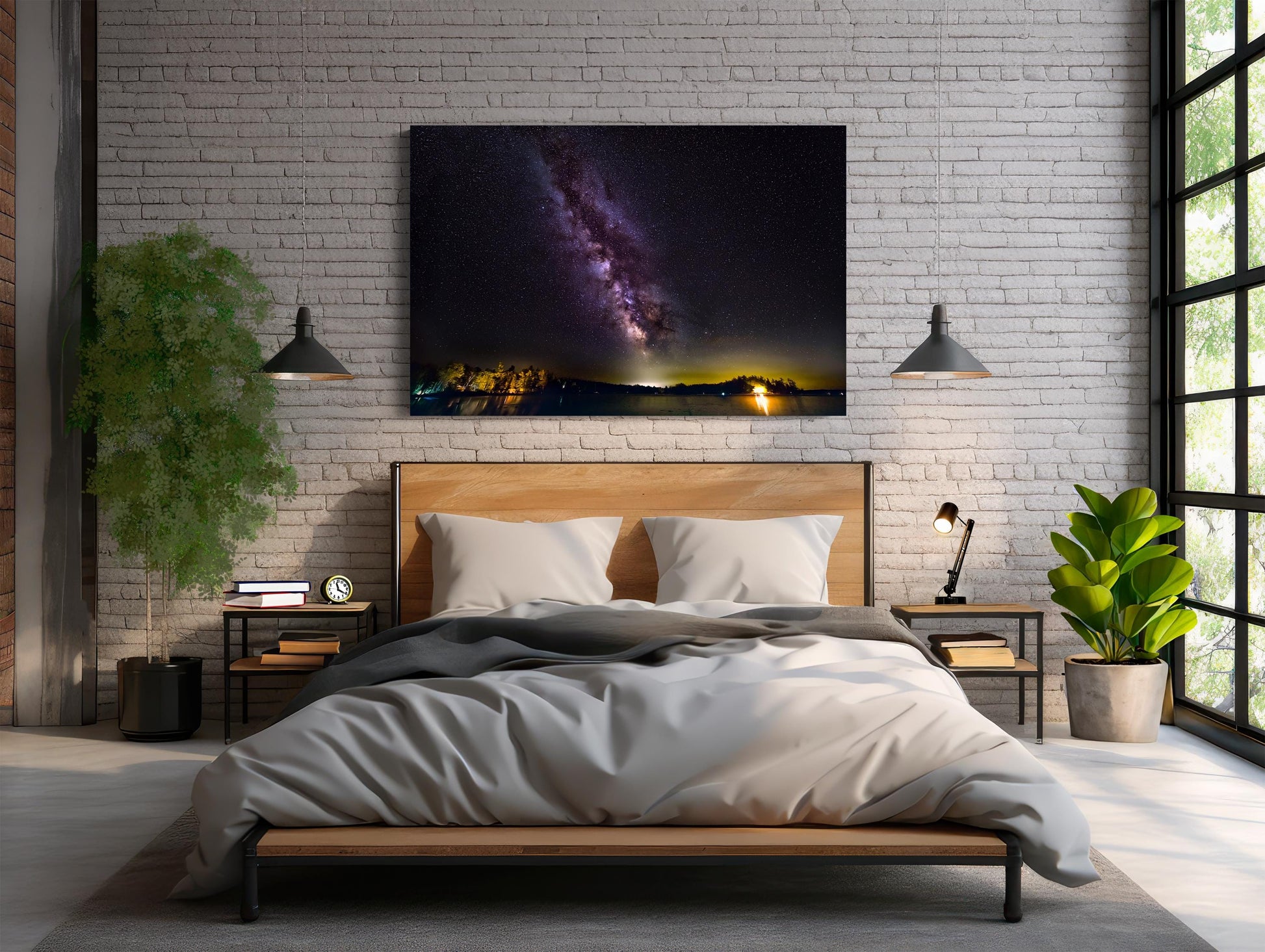 A vivid Milky Way core glows in a vertical sweep across a dark, starry night sky. The stars and galactic dust create a textured ribbon of light. Below, a calm lake mirrors faint reflections of the stars, with a rocky shoreline in the foreground and a glowing island of trees lit in the distance.